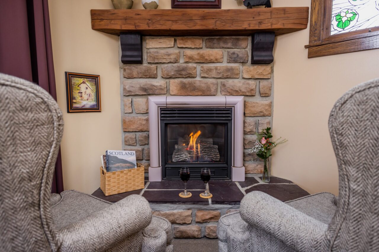 Picture of two chairs facing the fireplace, with two glasses on wine on the mantel.