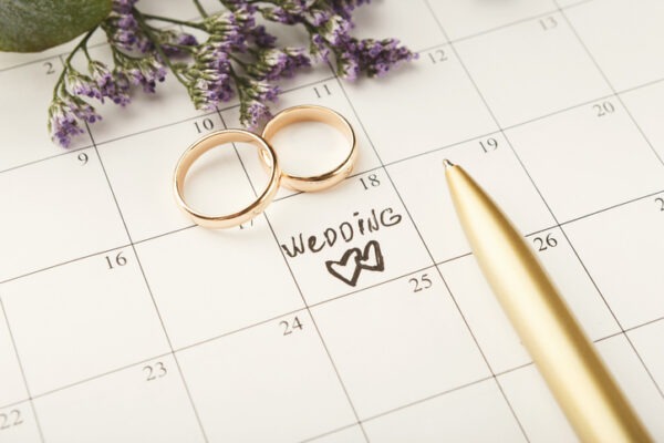 Word wedding, two hearts and gold rings on calendar with sweet purple flowers. Love, invitation, advertisement, romantic background concept, copy space