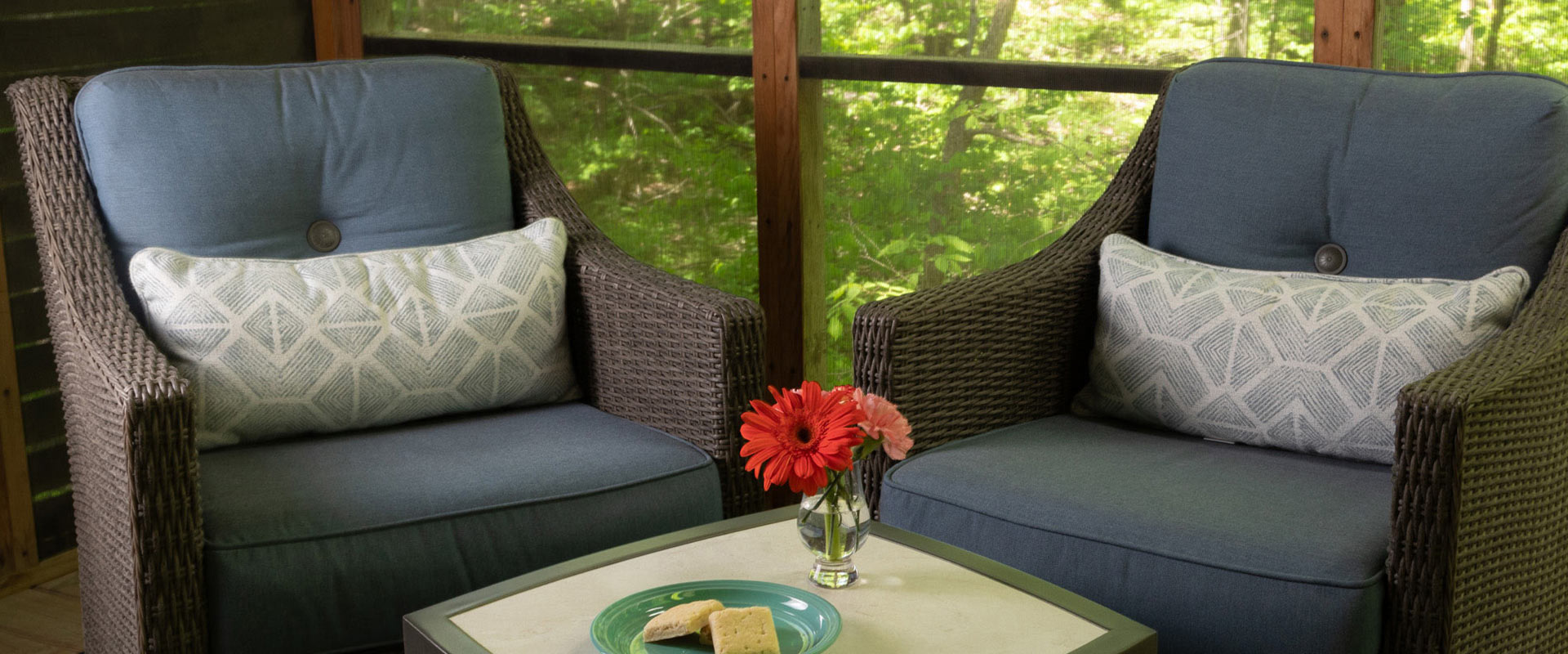 Picture of two chairs, with a table in the middle, topped with a plate of shortbread cookies and a vase of flowers.