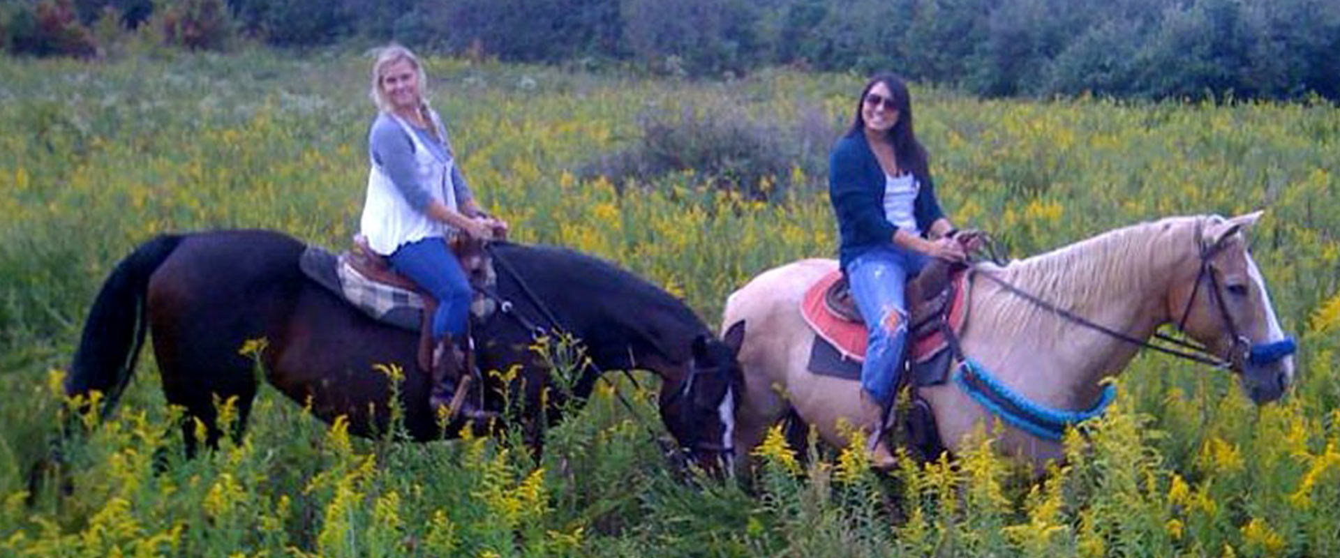 Two women horseback riding in a field of wild flowers.