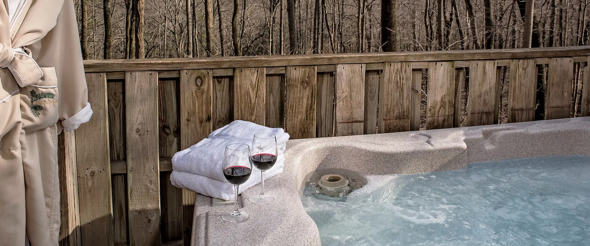 Two glasses of red wine next to towels and a hot tub.