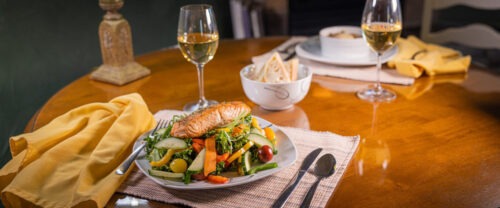 Salmon on a plate of greens, with glasses of wine.