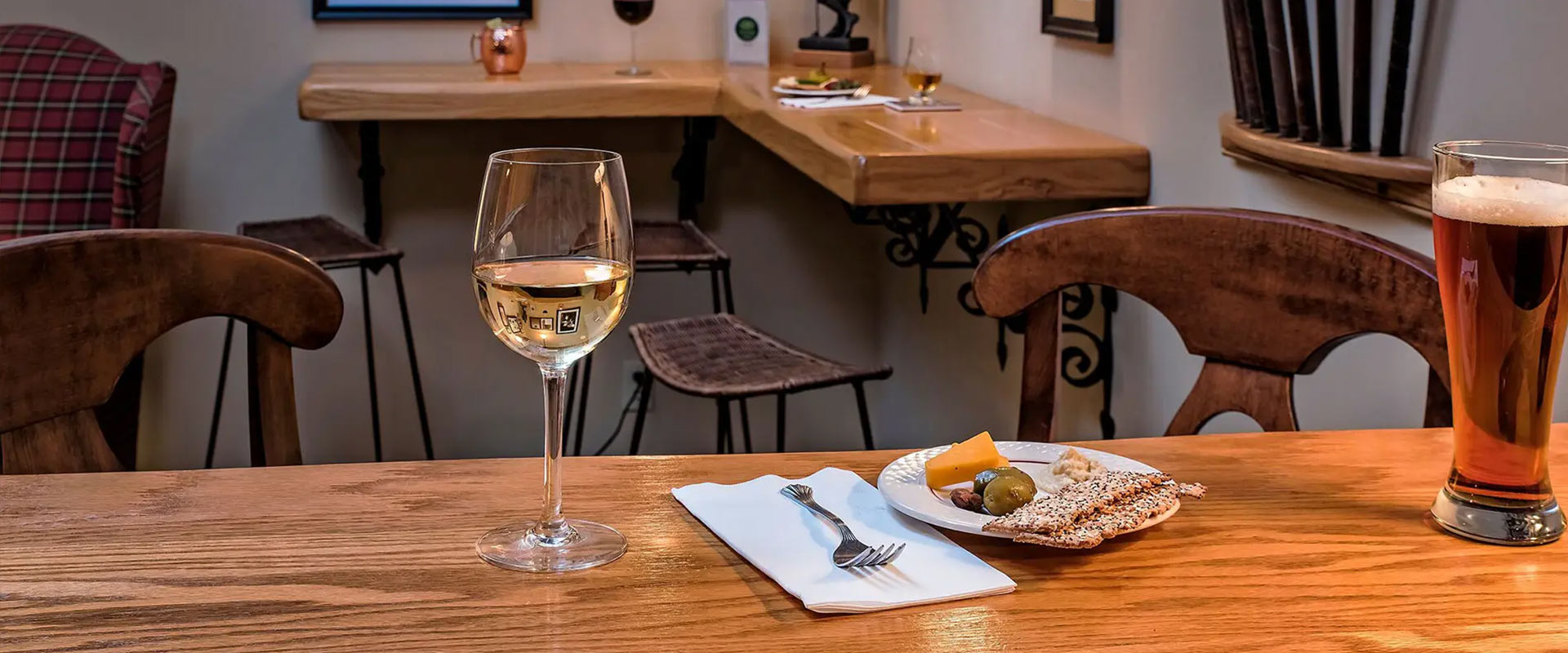 Glass of wine and beer, near a snack plate.