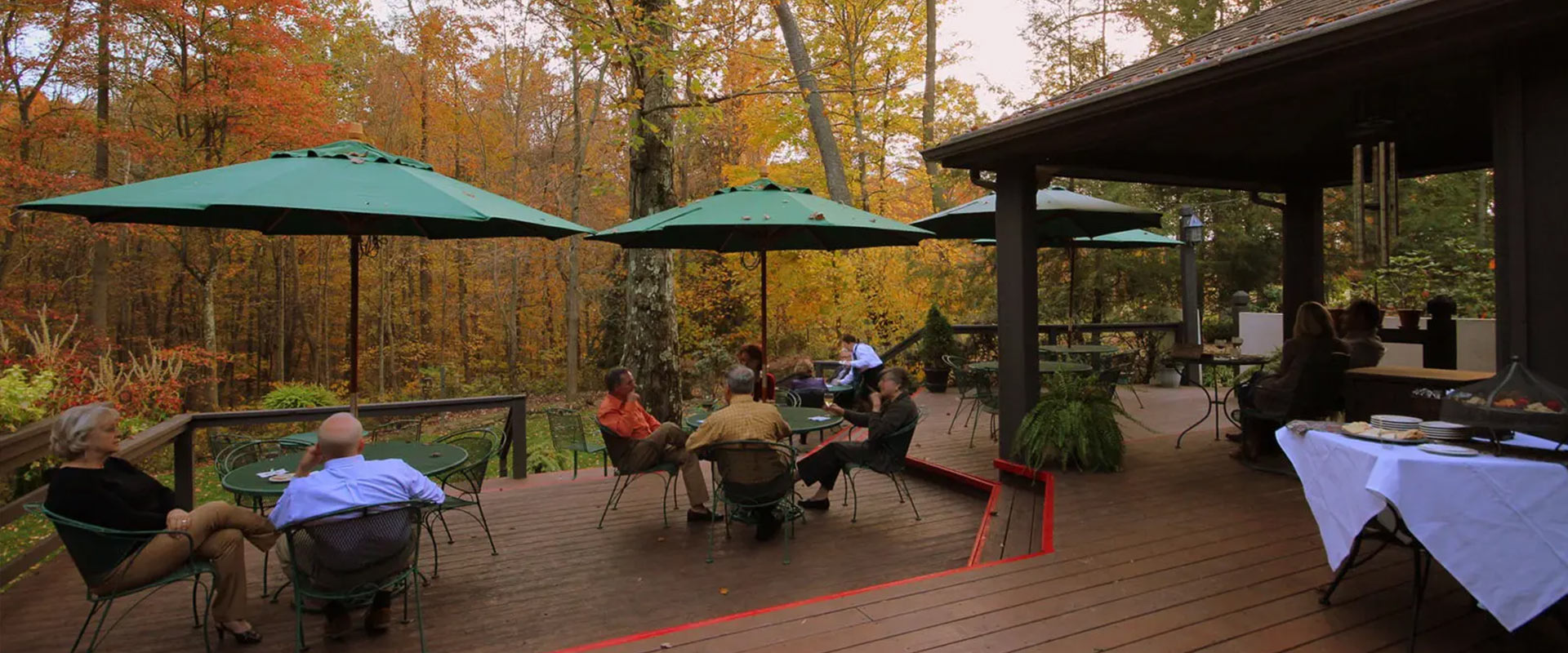 Patio with green umbrellas, surrounded by fall-colored trees.